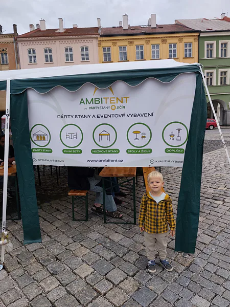 Chlapec pred zeleným stanom s bannerom Ambitent na festivale v Jičíne.